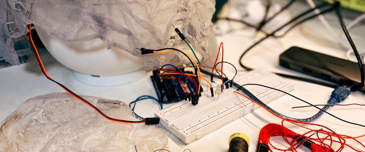 Art fabrication in progress, with a micro-controller connected to white mesh material on a white desk
